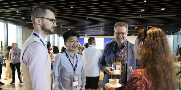 A group of people engaging in conversation at a networking event, holding coffee cups and wearing name tags.