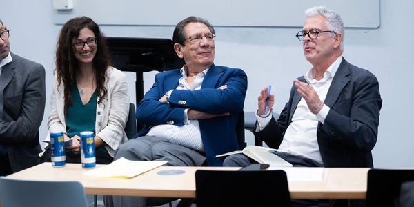 A panel discussion featuring three individuals sitting at a table, engaged in conversation.