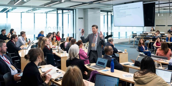 A man is giving a presentation in a modern classroom filled with engaged participants.
