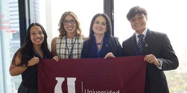 A group of four people holding a university banner in an office setting.