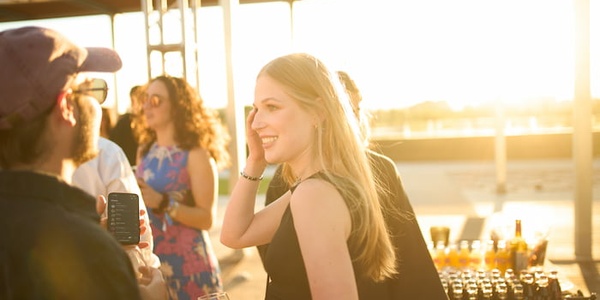 A woman smiling and engaging in a conversation at an outdoor party during sunset.