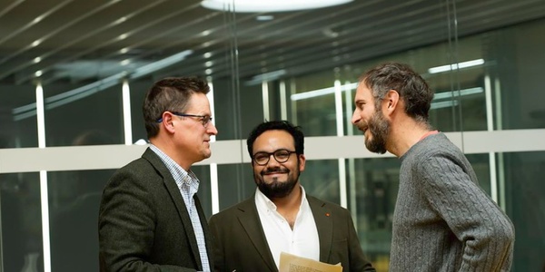 Three men in a business setting, casually interacting and smiling.