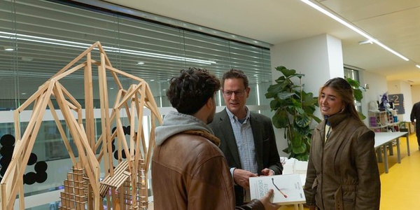 Three people discuss a model bridge in an office environment.