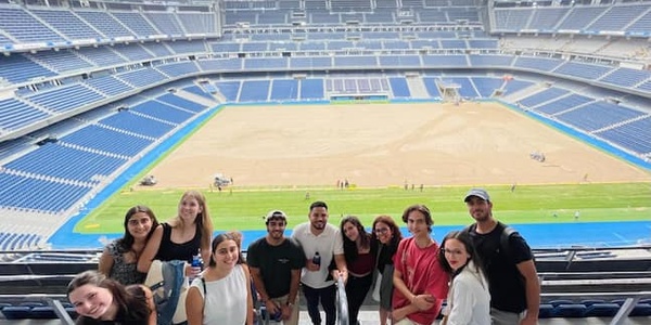 A group of people smiling and posing for a photo in a large, empty stadium with ongoing construction in the field.