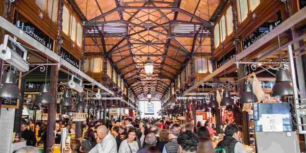 A bustling market hall filled with people and various food stalls.
