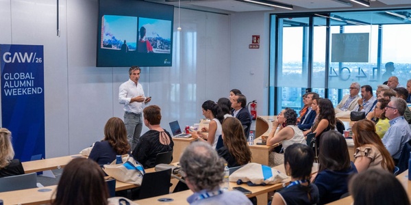 A speaker presents during a conference with an audience seated in a modern room.