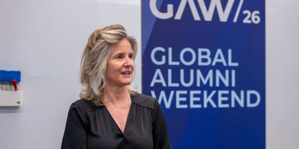 A woman is speaking at an event labeled Global Alumni Weekend.