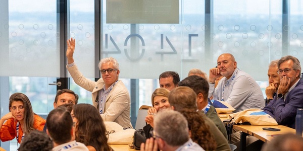 A group of people engaged in a meeting, with one individual raising their hand to speak.