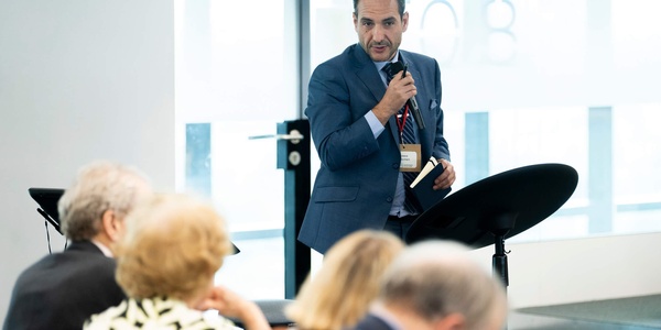 A speaker presents at a university event while an audience listens attentively.