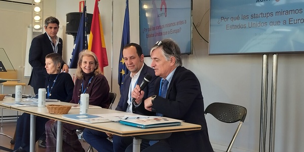 People seated at a panel discussion in a conference room with banners and a projector screen.
