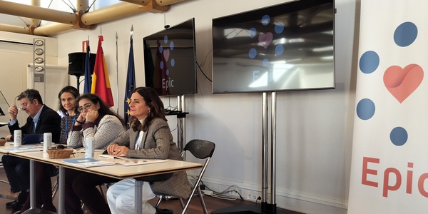 A group of people sitting at a long table during a panel discussion in a room with banners displaying logos.