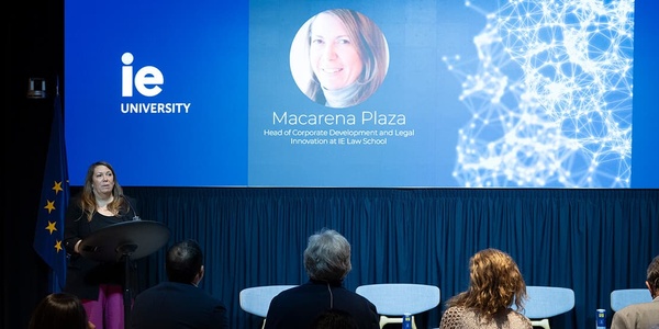 A woman is speaking at a podium in front of a presentation screen at an educational event.