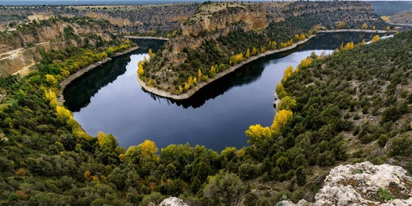 A picturesque view of a winding river surrounded by lush greenery and autumn-colored trees.