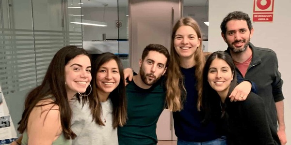 A group of six young adults smiling and posing together in an office environment.
