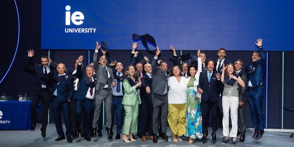 A group of people celebrating together at an event with IE University branding in the background.