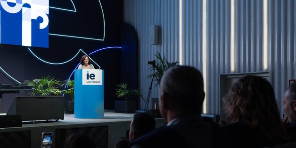 A speaker presents on stage at an event hosted by IE University.