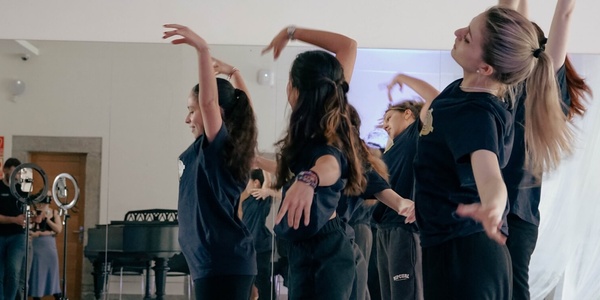 A group of dancers practicing in a studio with a piano in the background.