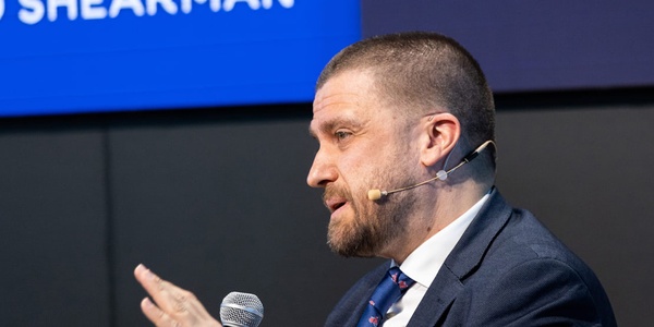A man in a suit is speaking into a microphone at a conference.