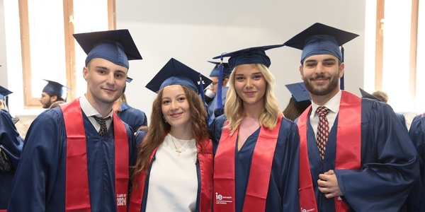 Four graduates in blue and red regalia smiling at a graduation ceremony