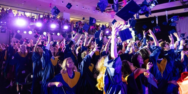 A large group of graduates celebrating and throwing their caps in the air at a graduation ceremony.
