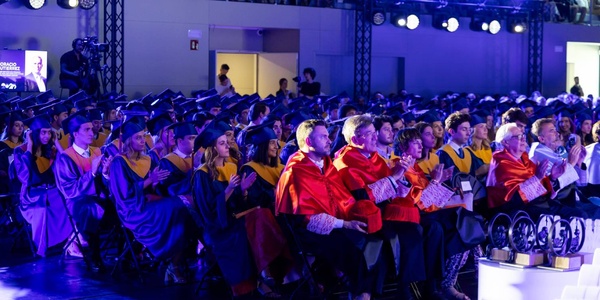 A group of graduates sitting in a ceremony wearing robes and caps.