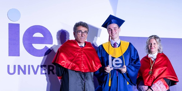A graduate in a cap and gown stands proudly between two individuals, celebrating at a university event.