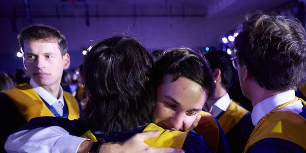 A moment of graduates celebrating together with hugs during their graduation ceremony.