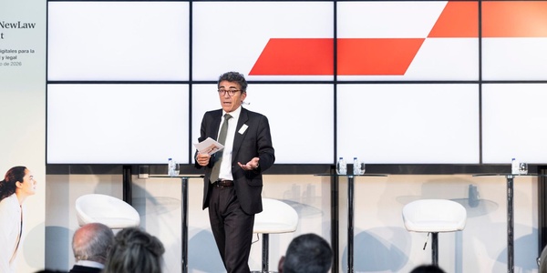 A speaker presents at a business conference with a modern backdrop.
