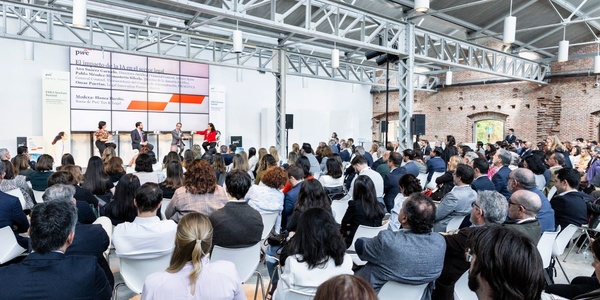 A large audience is gathered at a seminar featuring a panel discussion in a modern venue.