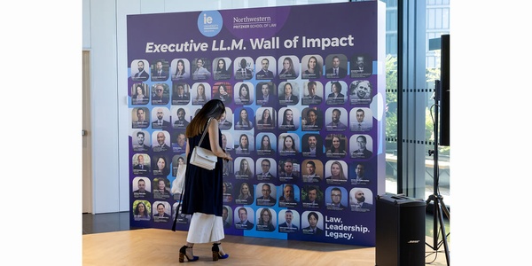 A woman is observing a wall filled with headshots representing the Executive LL.M. program.