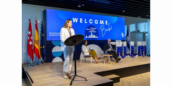 A speaker addressing an audience at a welcome event with flags in the background.