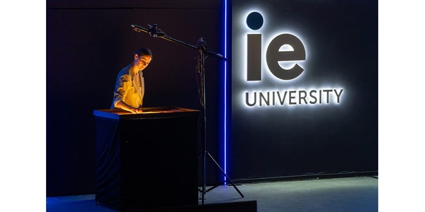 A person is presenting in front of the IE University sign.