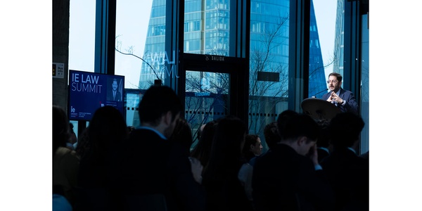 A speaker addresses an audience at a law summit held in a modern venue with large windows.