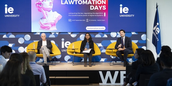 Three professionals sitting on a panel at a conference event, discussing topics in front of an audience.
