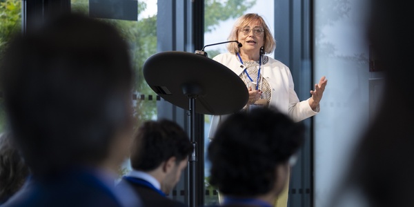 A woman is giving a speech at a podium in a conference room, addressing an audience.