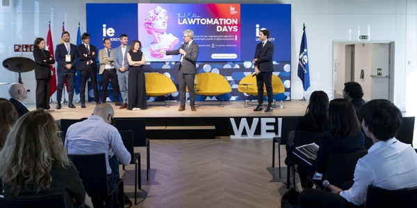 A group of people standing on a stage during an event titled 'Lawtomation Days' at a venue with audience members seated facing them.
