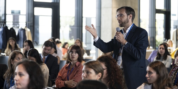 A man in a suit is speaking into a microphone in front of an audience at a conference.