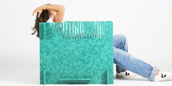 A woman sits behind a large turquoise shopping bag, her face obscured and only her arms and legs visible.