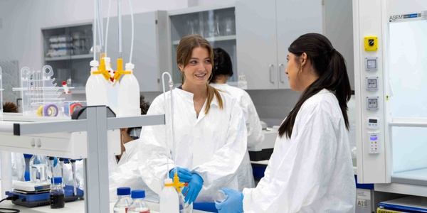Two women in lab coats are engaged in conversation while working in a laboratory.