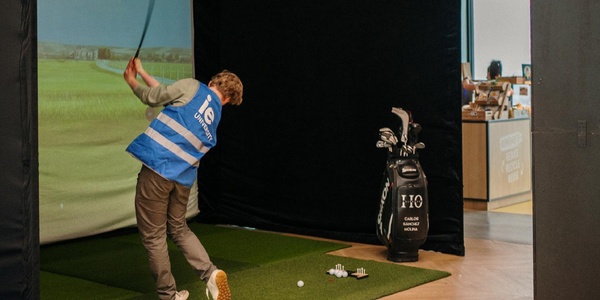 A person is golfing indoors, swinging a club in front of a simulator screen.