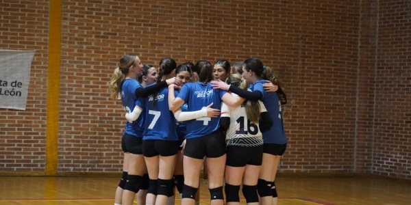 A group of young female volleyball players huddled together in a gym.