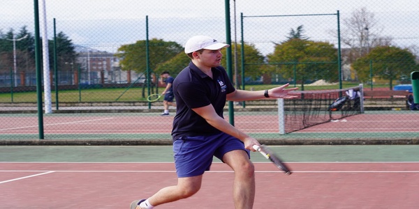 A young man is playing tennis on an outdoor court.
