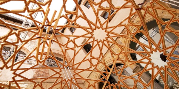 A complex geometric ceiling structure made of interlocking wooden beams.