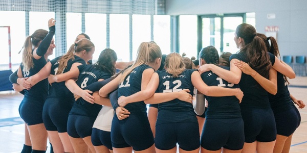 A group of young female volleyball players huddled together in a supportive formation.