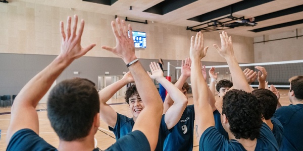 A group of young volleyball players celebrating with their hands raised.