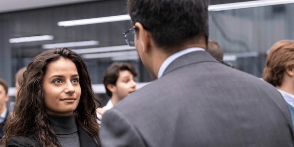 A young woman and a man in a business suit having a conversation in a busy office environment.