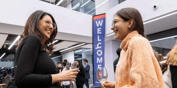 Two women smiling and talking at a welcome event in a modern office space.