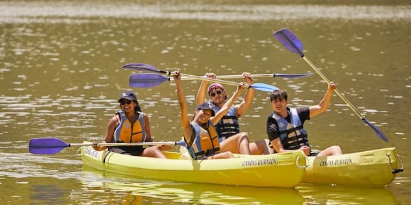 Three people joyfully kayaking on a calm river, waving and smiling.