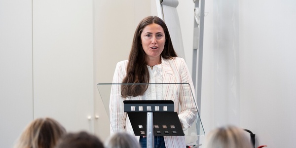 A woman is giving a speech at a podium in front of an audience.