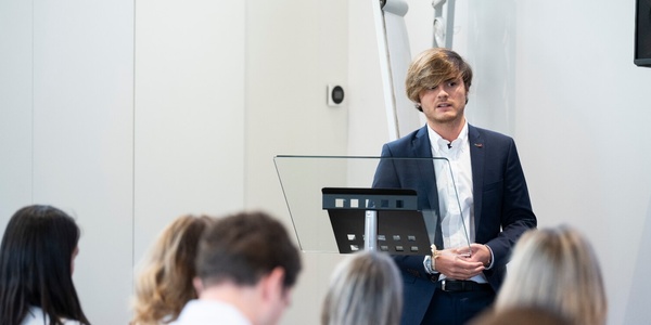 A man with glasses presenting in front of an audience at a seminar.